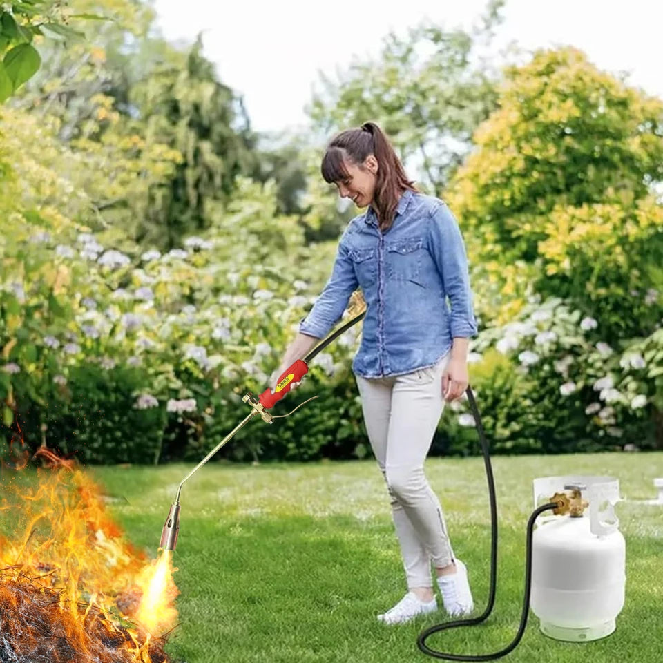 Close-up of a portable manual igniter with a gas hose attachment, shown in an outdoor setting (view 2)