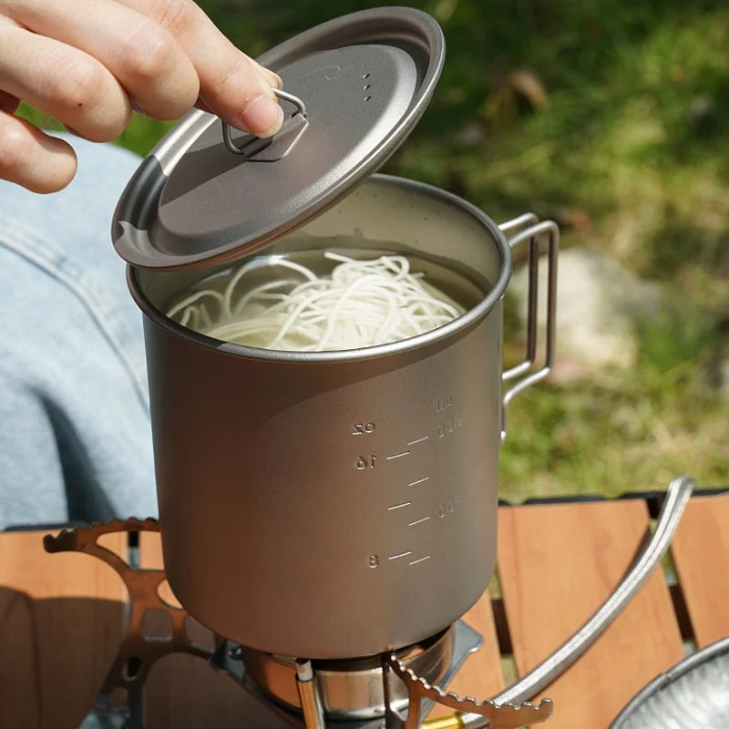 Titanium camping mug with a folding handle, shown in an outdoor setting (view 5)